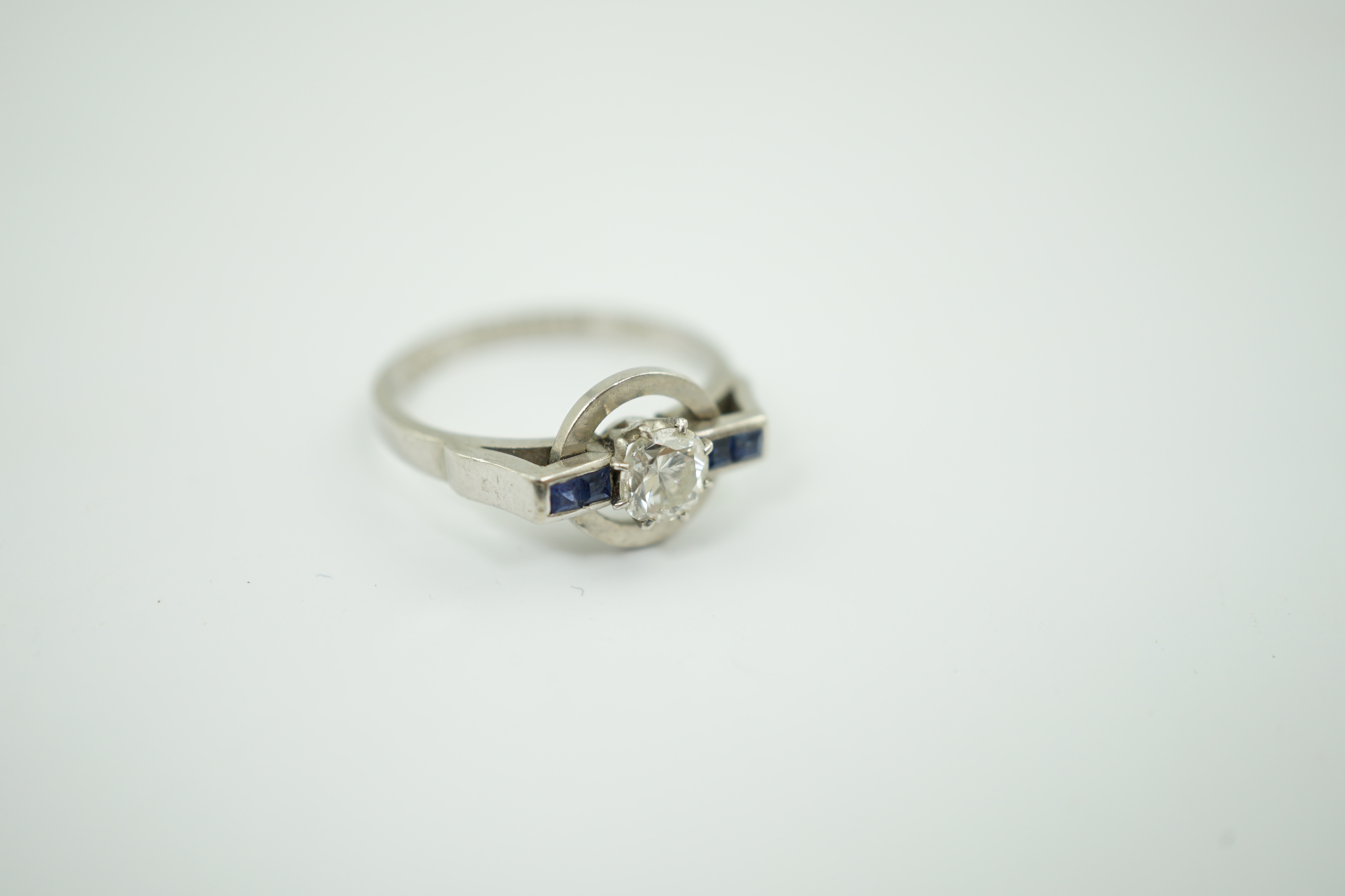 A platinum and single stone diamond set target ring, with four stone square cut sapphire set shoulders